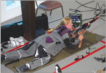 Air rifle shooter Morgan Sitra from a prone position prepares to fire at a target. Note the electronic target tracking system near her face.