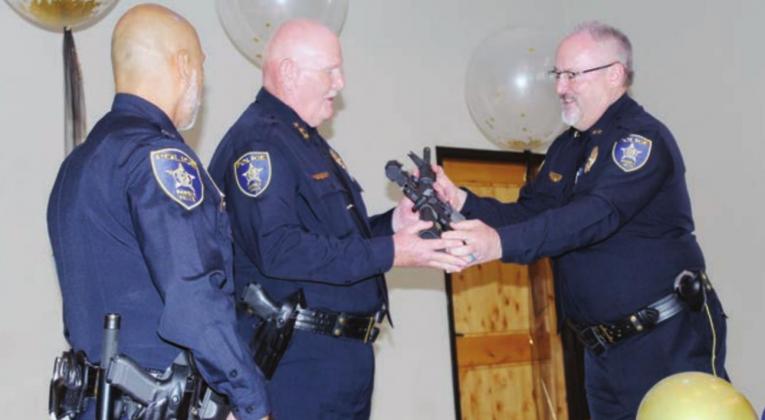 Right: Marble Falls Assistant Police Chief Glenn Hanson, right, presents an AR-15 to retiring Marble Falls Police Chief Mark Whitacre, center, while Capt. Robert Talamantes looks on.