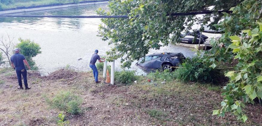 Gerrad Cranfill, left, looks back to make sure the car in Lake LBJ he tied up to a tree is still secure while an unidentified City of Horseshoe Bay staffer checks out the damage done to a post at the water’s edge. Cranfill is credited with helping extract a motorist from the car after it went off FM 2147 into the water on June 15. Lew K. Cohn/The Highlander